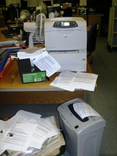 Computer printouts overflowing into a wastepaper basket and a shredder